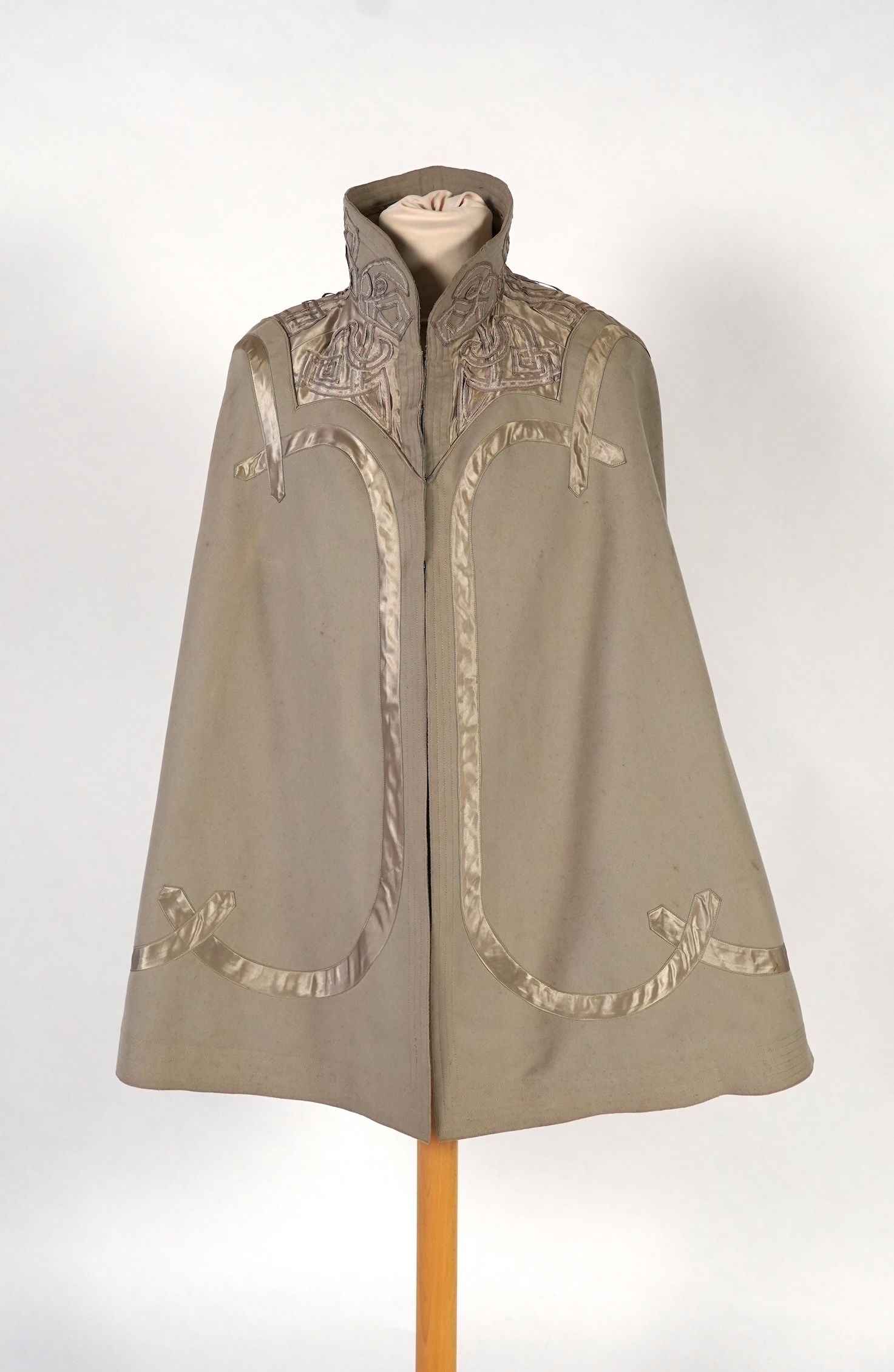 An Edwardian mushroom wool evening cape, decorated with silk ribbon worked strapping and ornate appliquéd fine braiding across the shoulders and under section of the collar, lined with cream silk satin.